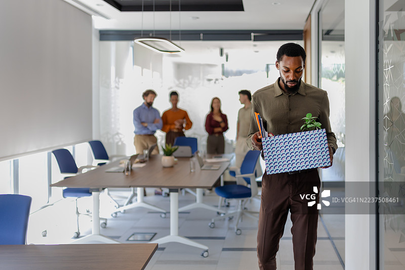 辞职概念：一位黑人男性带着办公必需品的箱子离开工作岗位图片素材