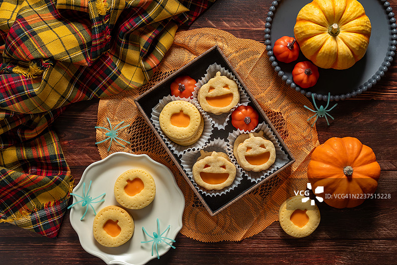 万圣节南瓜形状的三明治饼干，夹有甜奶油馅，背景为深色木材。杰克南瓜饼干。图片素材