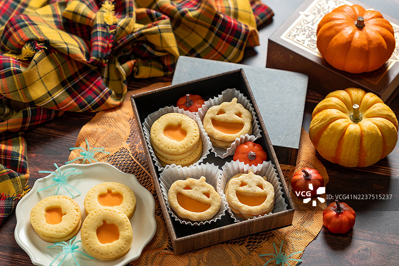 万圣节南瓜形状的三明治饼干，夹有甜奶油馅，背景为深色木材。杰克南瓜饼干。图片素材