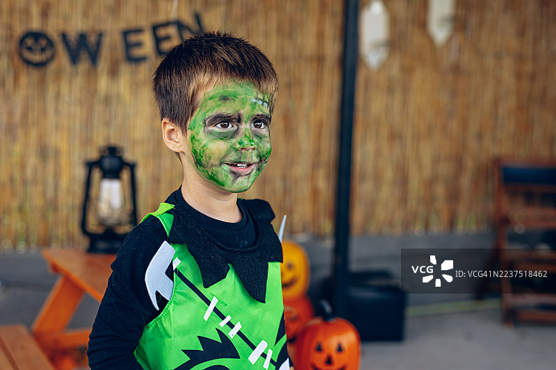 孩子在万圣节庆祝活动中，享受着糖果，脸上化着恐怖的弗兰肯斯坦风格妆容。图片素材