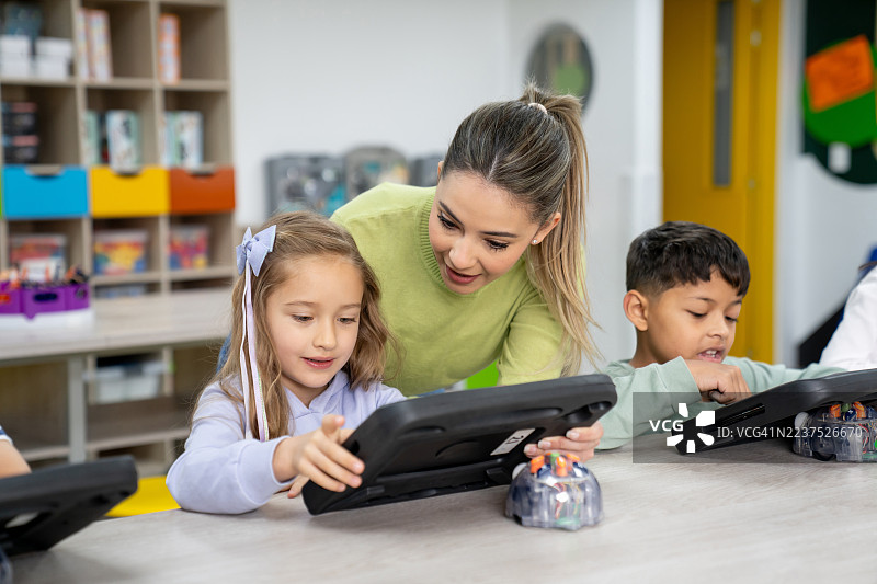 女孩在老师的帮助下，在学校的STEM课堂上学习编程。图片素材
