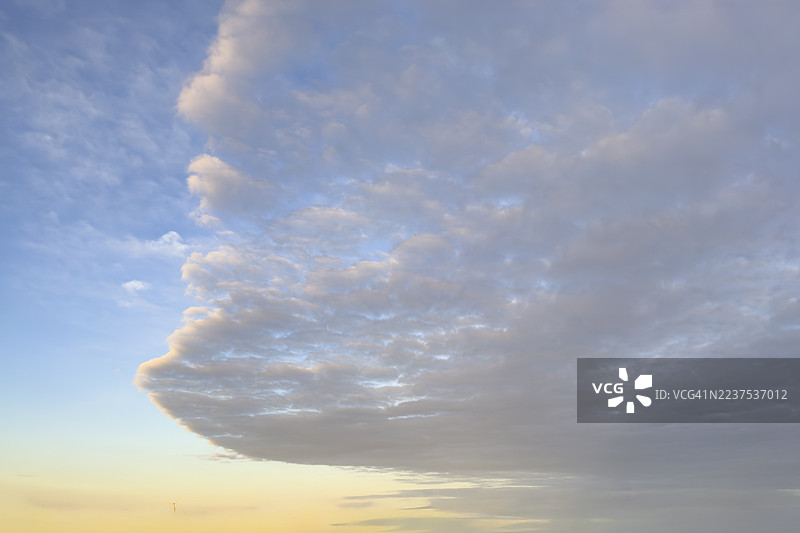 云锋，下方有层积云。层积云呈动态弧形，上方有高积云。蓝天下有层积云聚集，背景是金色的傍晚天空，临近黄昏，国际。图片素材