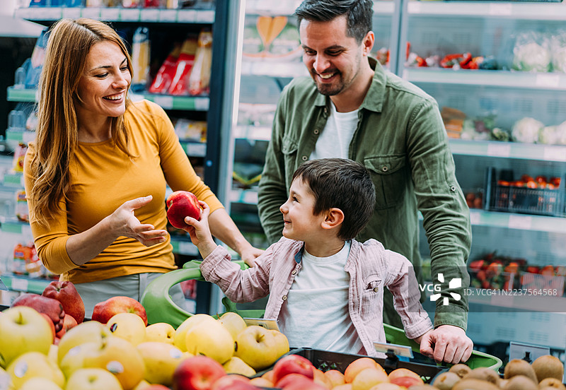 微笑的家庭在超市里推着购物车挑选商品。图片素材