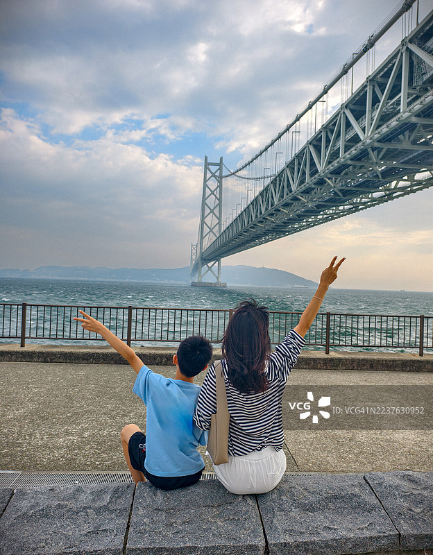在中国神户，一个中国孩子和他的母亲在明石海峡大桥下玩耍图片素材