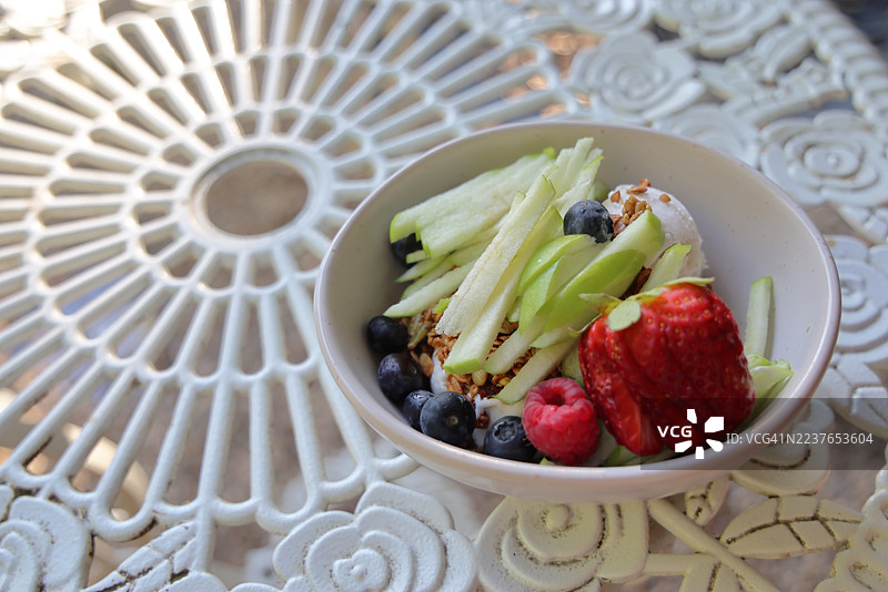 杏仁枫糖燕麦格兰诺拉麦片、冷冻椰子酸奶以及新鲜水果（草莓、史密斯奶奶苹果、蓝莓和覆盆子），摆放在白色的锻铁桌面上。图片素材