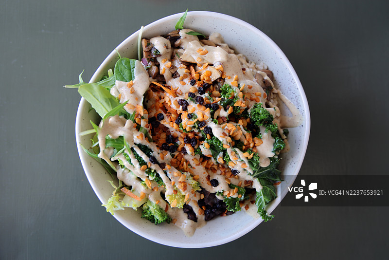 椰子糙米饭沙拉碗，配有沙拉蔬菜、红豆、胡萝卜、西兰花、羽衣甘蓝、香菇、黑豆、黑加仑、烤大蒜夏威夷果和柠檬芝麻酱沙拉酱图片素材