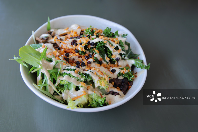 椰子糙米沙拉碗，配有沙拉菜、芸豆、胡萝卜、西兰花、羽衣甘蓝、香菇、黑豆、醋栗、烤大蒜夏威夷果和柠檬芝麻酱沙拉酱图片素材