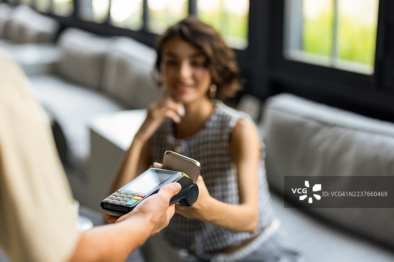 女性使用手机无接触支付应用在咖啡店支付账单。图片素材