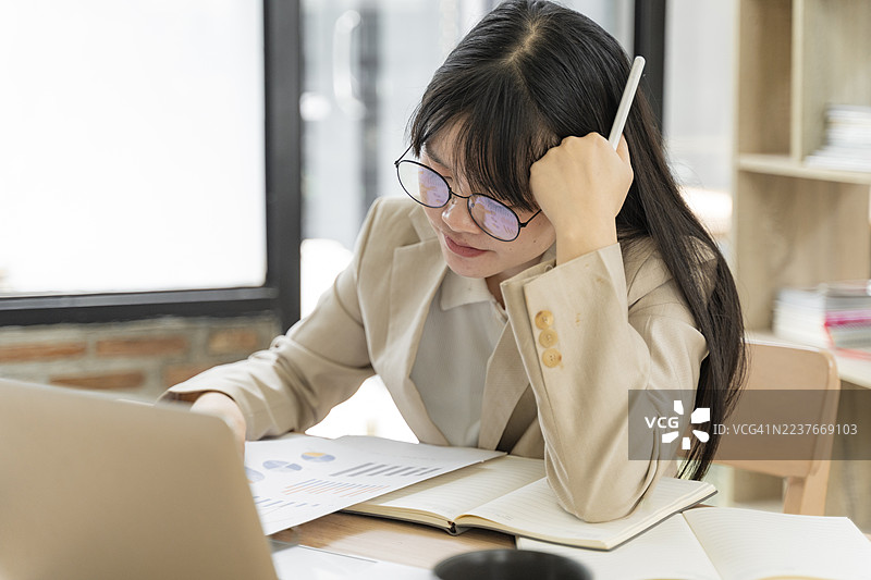 过度劳累的年轻东亚女性（20至30岁）专业人士在亚洲分析文件并加班。图片素材