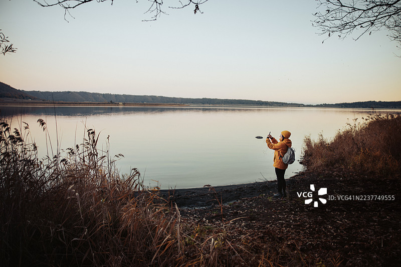 女子在湖边拍摄秋季风景照图片素材