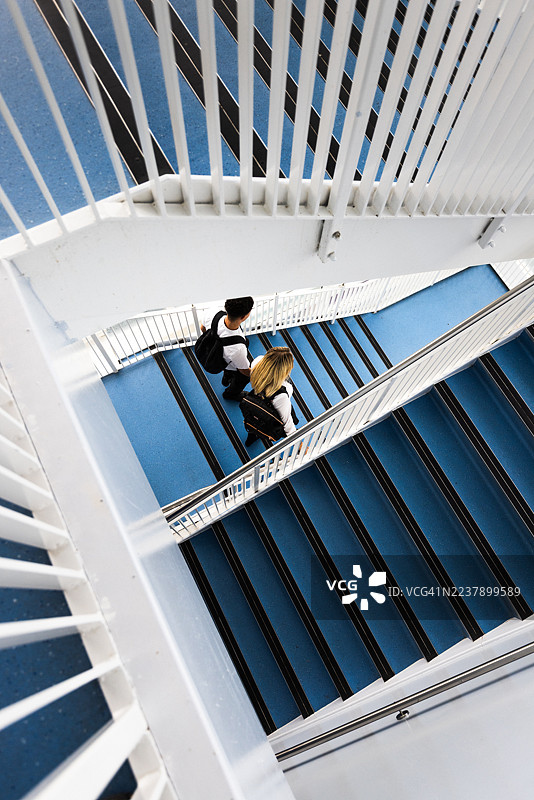 从高角度拍摄的英国高中楼梯，两名十几岁的学生并排走下楼梯，地点为英国纽卡斯尔。图片素材