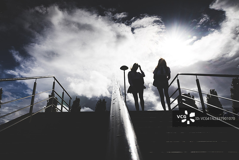 低角度拍摄，向上看，两名女高中生剪影在英国纽卡斯尔纽卡斯尔纽卡斯尔大学校园的户外台阶顶部聊天。图片素材