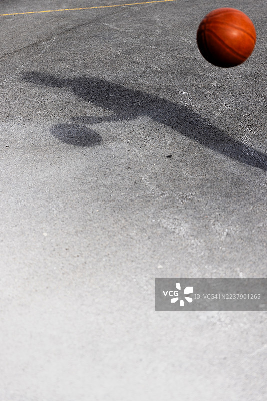 一名十几岁的男性在沥青运动场上拍着篮球,这是在一个阳光明媚的下午,纽卡斯尔联,英格兰,英国的一所高中课间休息时拍摄的。图片素材