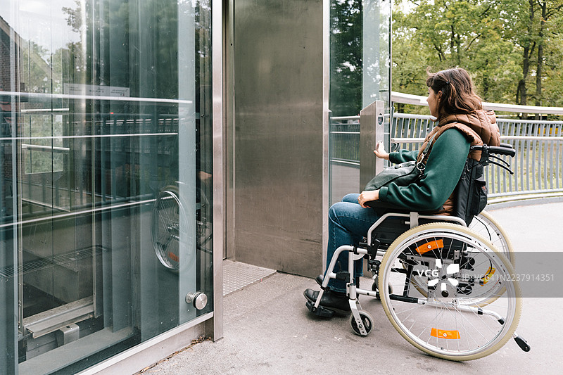 一位女性按下轮椅升降机的按钮以便使用公共交通。图片素材