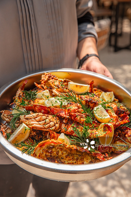 厨师手持平底锅，准备新鲜的海鲜，包括龙虾、香草烤制和蒜香虾，阳光明媚的户外餐厅为烧烤派对增添气氛。图片素材