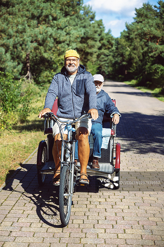 阳光明媚的一天，一位友善的男士正驾驶着一辆漂亮的载客三轮车，载着一位长者。图片素材