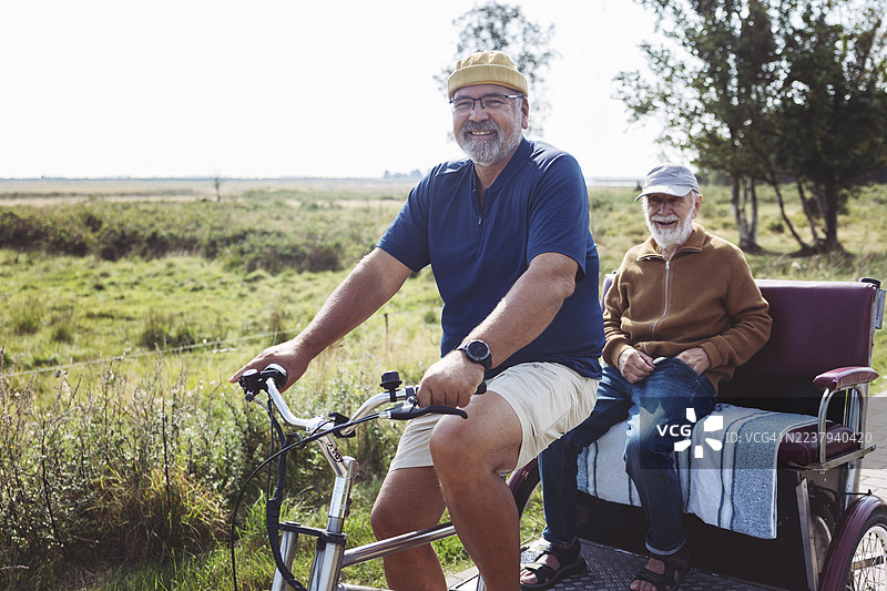阳光明媚的一天，一位友善的男士开着一辆漂亮的电动三轮车，载着一位年长的女士。图片素材