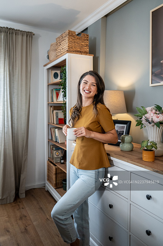 女人在舒适的家中开心地笑着，享受着咖啡。图片素材