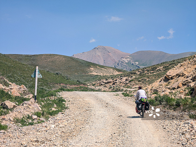 独自骑行者，装备着自行车旅行装备，在吉尔吉斯斯坦的偏远地区，沿着一条蜿蜒穿过广阔山景的砂石路，开启一段充满冒险的旅程。图片素材