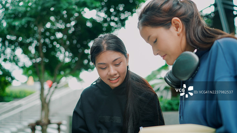年轻的亚洲大学生在校园里坐着比较笔记。图片素材