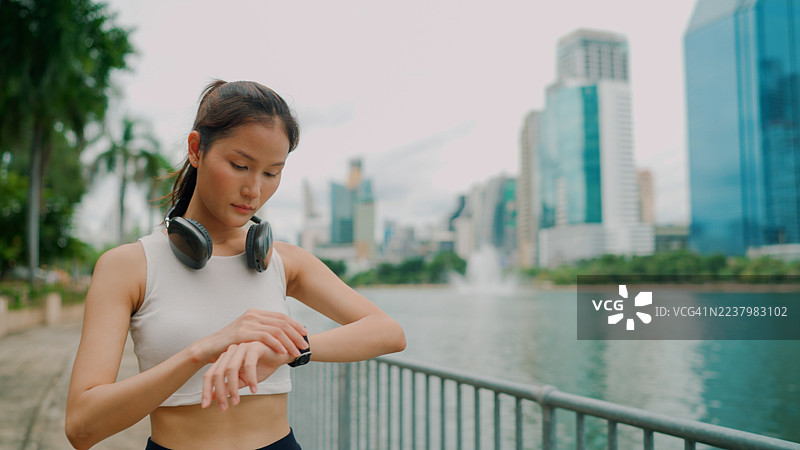 年轻的亚洲女性在公共公园跑步后，查看她的智能手表以了解锻炼进展。图片素材