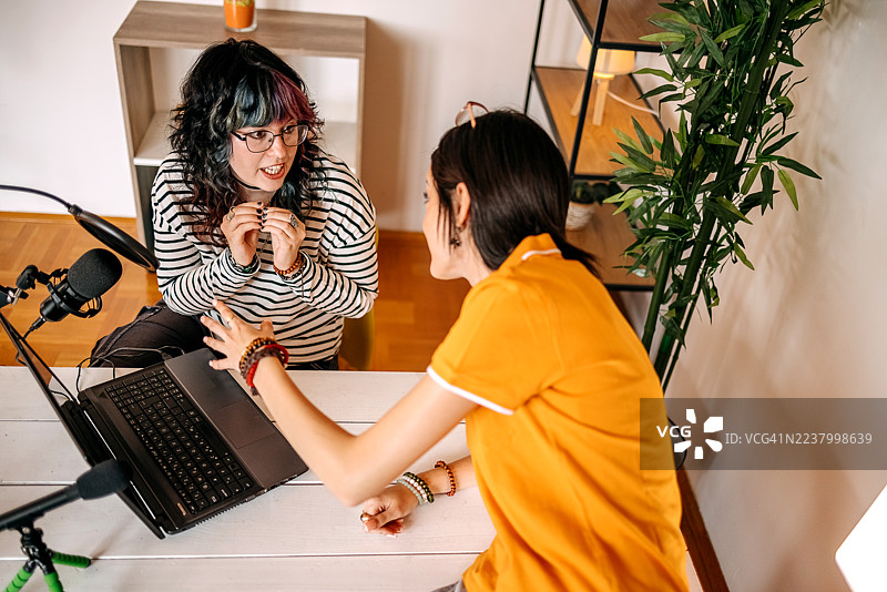 几位女性朋友在家录制播客，其中一人坐在桌子上。图片素材