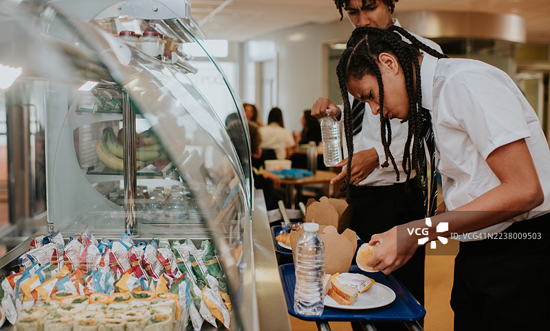 一个男孩在自助餐厅排队时查看三明治，神情困惑。图片素材