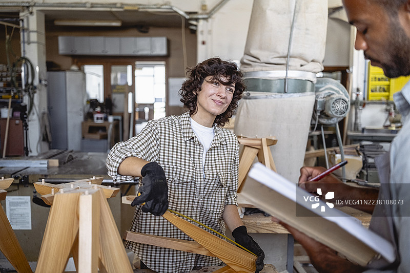 不同肤色的男女木工在车间合作，进行测量和记录。图片素材