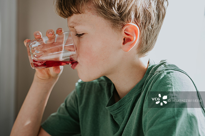 男孩在通风、明亮的室内喝稀释的果汁图片素材
