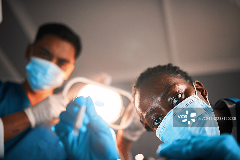 两位戴着口罩的牙医在明亮的牙科灯下，于牙科诊所内使用器械工作图片素材