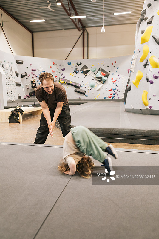 一位父亲在攀岩中心帮助女儿做空翻。图片素材