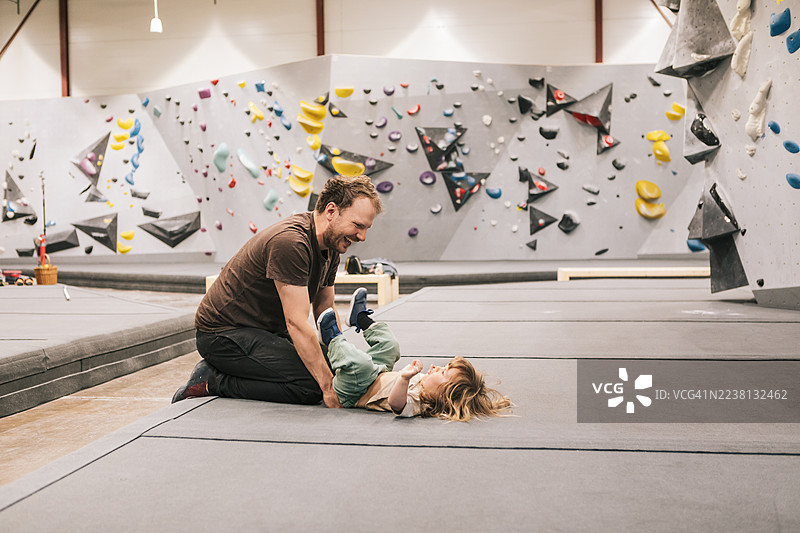 一位父亲在育儿假期间，带着他的小女儿在室内攀岩中心玩耍。图片素材