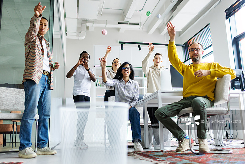 同事们在工作中用纸团和垃圾桶玩篮球放松图片素材