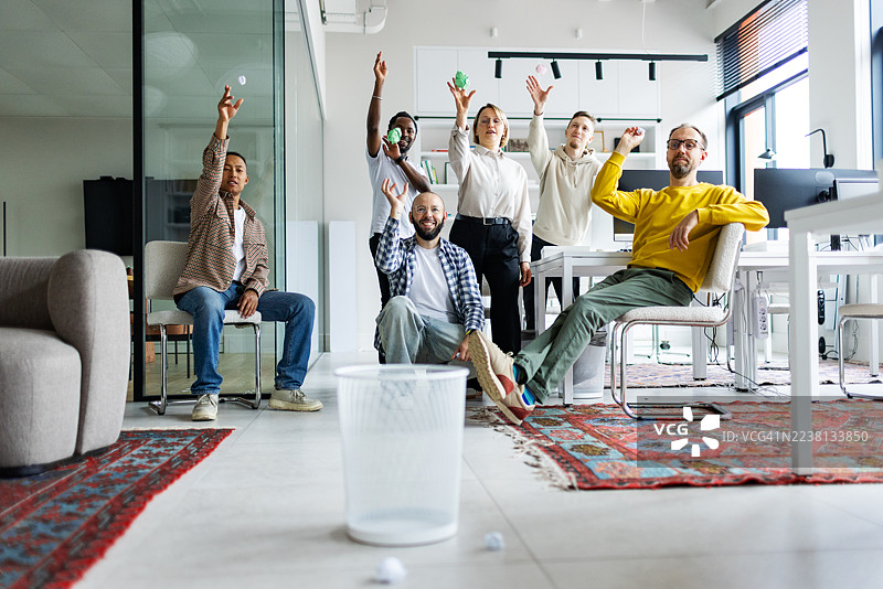 同事们在工作中放松，用纸团和垃圾桶玩篮球。图片素材