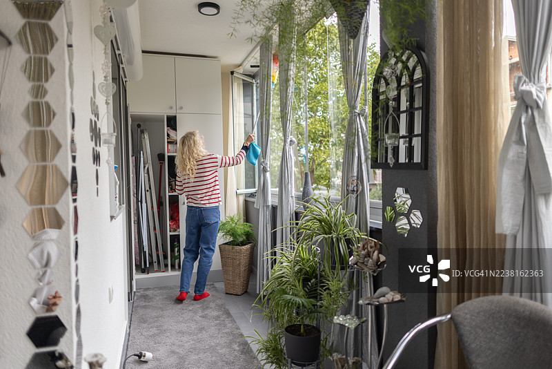 明亮家居中，女人在带植物的舒适室内空间里清洁阳台窗帘图片素材
