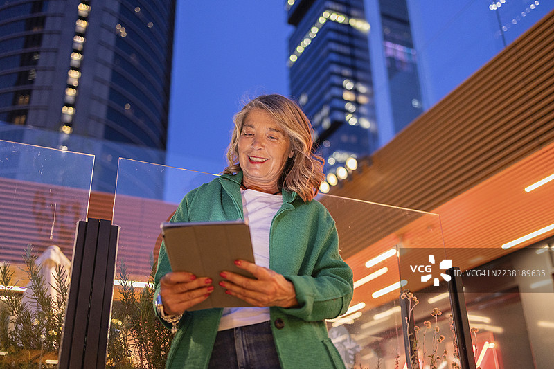 微笑的女性在城市街道上傍晚时分使用平板电脑图片素材