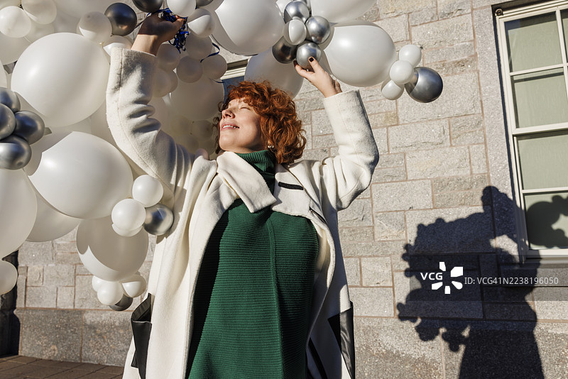 气球魔法在城市街道上。快乐的红发女子在纽约州麦迪逊的街道上与气球共舞。图片素材