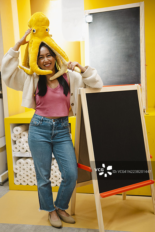 微笑的女性在室内摆姿势，身穿黄色帽子，旁边有一块空白的黑板。图片素材