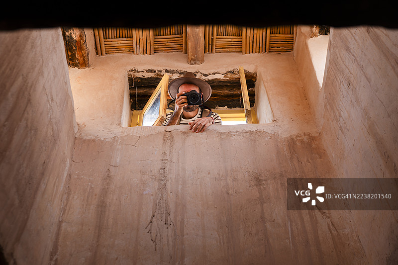 戴着帽子的男性摄影师通过历史建筑的窗户拍照图片素材