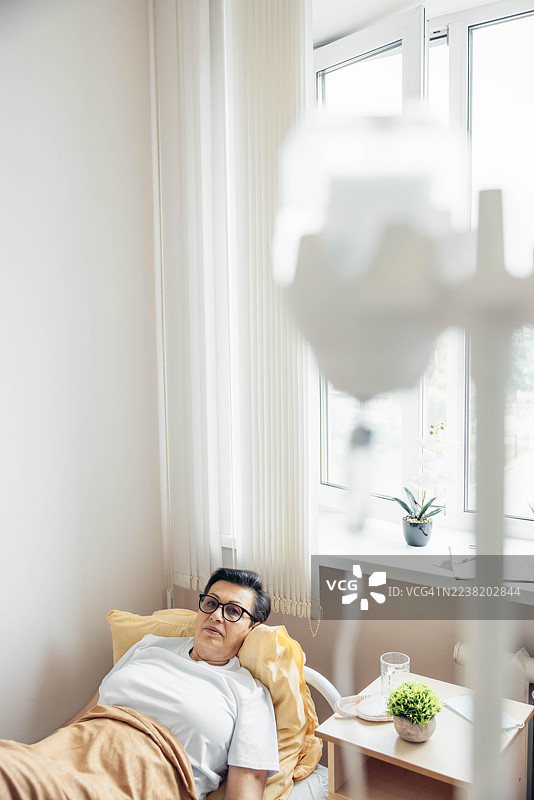 病人在医院床上休息，旁边有静脉输液，背景是窗户。图片素材