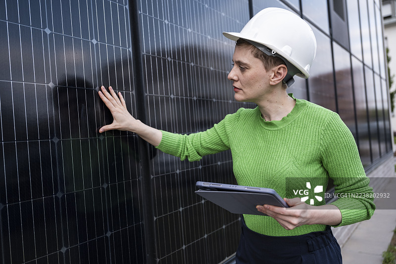工程师在户外检查太阳能面板墙，戴着安全帽图片素材