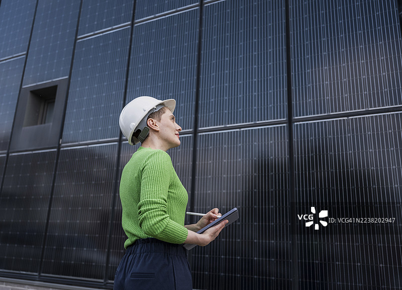 工程师戴着安全帽在户外使用平板电脑检查太阳能面板墙图片素材