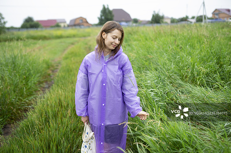 穿着紫色雨衣的女人在草地上享受夏季雨水图片素材