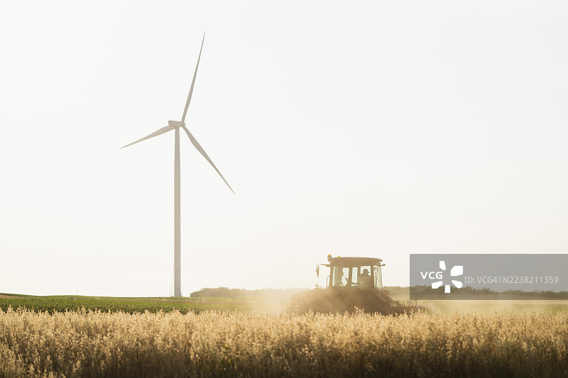 拖拉机在农田上工作，背景有风力发电机和可持续能源图片素材
