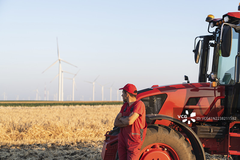 农民站在田野里的拖拉机旁，背景是风力发电机和蓝天。图片素材