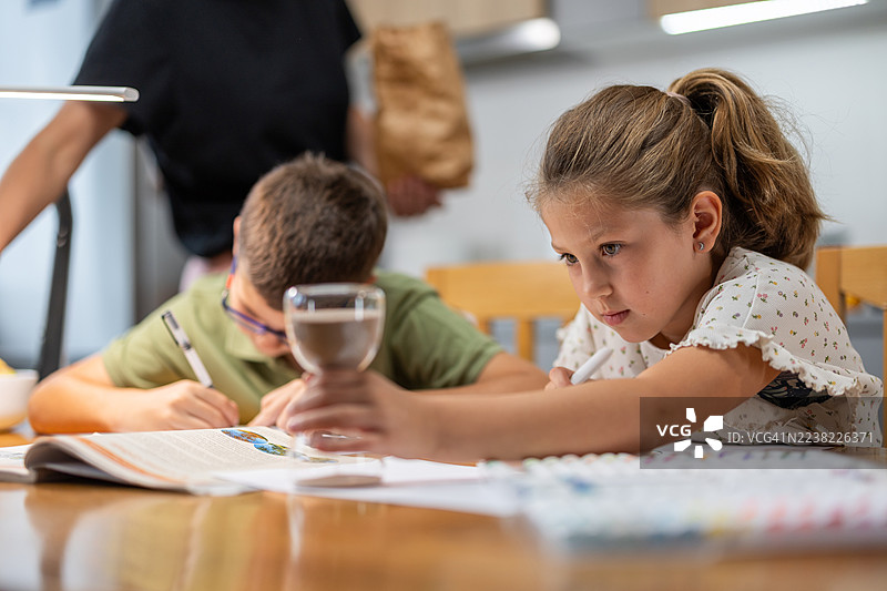 明亮的教室里，孩子们专注于在桌子旁学习和绘画。图片素材