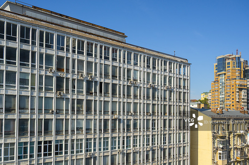 现代主义苏联时期办公楼外观与城市天际线中当代高层住宅建筑的对比，背景是晴朗的蓝天。图片素材