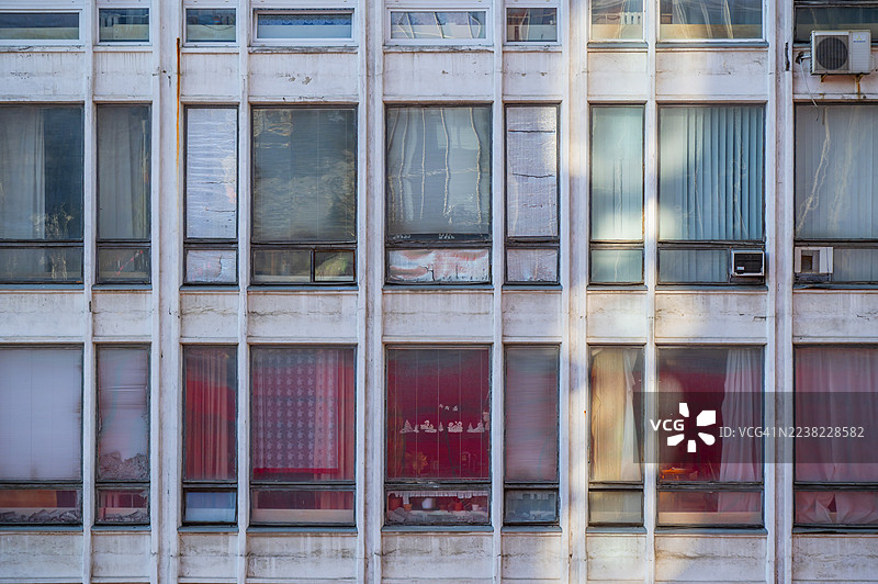 展示了风化混凝土网格的城市建筑立面，具有各种窗户和空调设备的几何图案，反映了城市生活中衰败和时光的流逝图片素材
