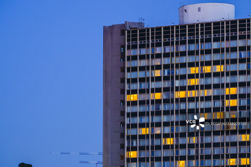城市企业摩天大楼的幕墙，有许多窗户，在黄昏时分，一些窗户被温暖的黄光照亮，代表着现代都市生活、商业和建筑概念。图片素材