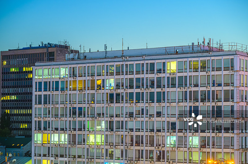 城市办公楼外墙，无数窗户倒映着蓝色时刻的天空和点亮的室内灯光，展示着黄昏时分的现代建筑和城市景观元素图片素材